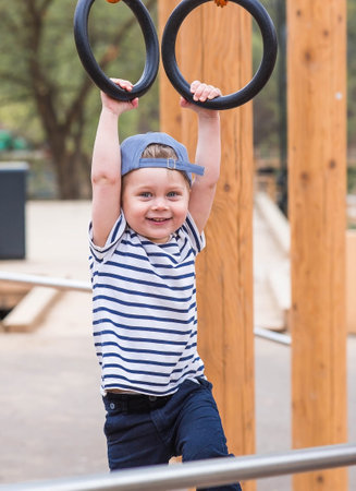 Lifestyle. A cute little boy is hanging on rings on a sports field in the fresh air. The concept of children's sports and physical development.の写真素材