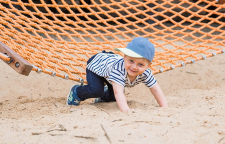 Summer lifestyle. A cute little boy is having fun playing in a hammock on the beach on a playground. The concept of family entertainment and leisure.の写真素材