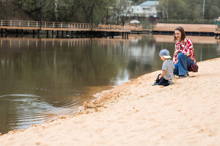 Summer lifestyle. A cute little boy and his mom are having fun playing with sand on the beach by the water. The concept of family entertainment and leisure.の写真素材
