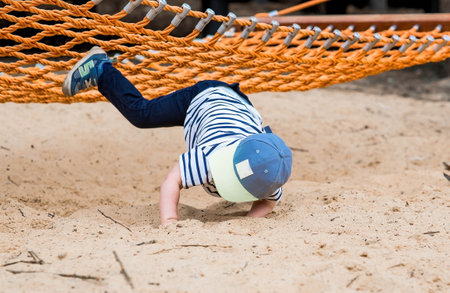 Lifestyle. Child safety. A cute little boy fell from a swing on a modern playground. The concept of caring for young children.の写真素材