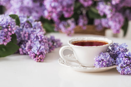 A cup of tea or coffee on the table. In the background is a large purple bouquet of lilacs. The concept of home comfort and drinks.の写真素材