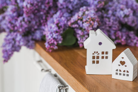 White Scandinavian houses on the kitchen countertop. In the background is a large purple bouquet of lilacs. The concept of home comfort and decor.の写真素材