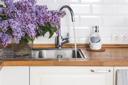 A large purple bouquet of lilacs in the sink or sink in the kitchen and lilac soap. In the background is the interior of a modern, stylish, bright kitchen. The concept of home comfort.の写真素材