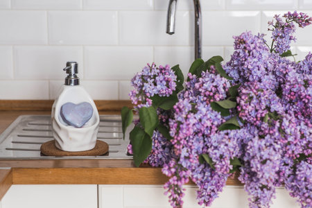 A large purple bouquet of lilacs in the sink or sink in the kitchen and lilac soap. In the background is the interior of a modern, stylish, bright kitchen. The concept of home comfort.の写真素材