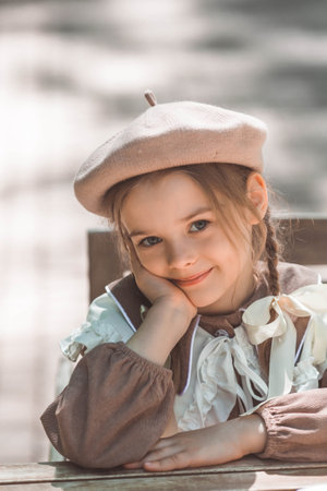 Vintage women's accessories and retro-style clothing. A small, beautiful girl with bows in her hair, in a beige dress and a beret outdoors.の写真素材