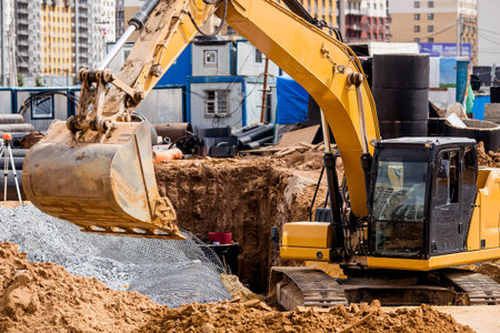 An excavator on a construction site in close-up. An excavator digs the ground with a bucket for...