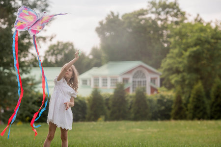 Children in the summer park. A beautiful girl is flying a kite in the fresh air. Warm family moments or a conceptual image for spending time outdoors.の写真素材