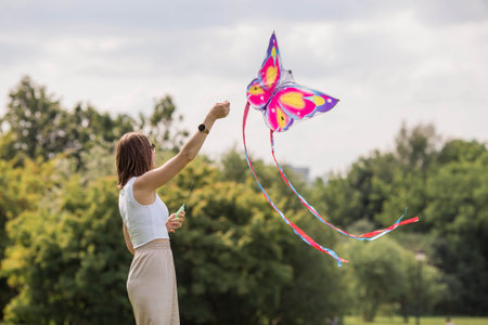 People in the summer park. A young woman flies a kite in the fresh air. Warm family moments or a conceptual image for spending time outdoors.の写真素材