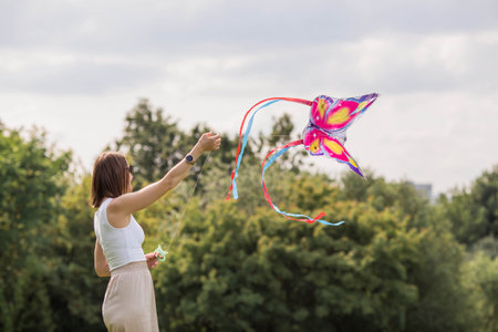 People in the summer park. A young woman flies a kite in the fresh air. Warm family moments or a conceptual image for spending time outdoors.の写真素材