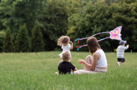 A family with three children. A mother with many children and toddlers in a summer park. Children are walking and flying a kite. Large families, family values, and leisure time with children.の写真素材