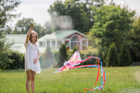 Children in the summer park. A beautiful girl is flying a kite in the fresh air. Warm family moments or a conceptual image for spending time outdoors.の写真素材