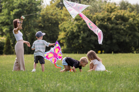 A family with three children. A mother with many children and toddlers in a summer park. Children are walking and flying a kite. Large families, family values, and leisure time with children.の写真素材