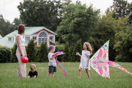 A family with three children. A mother with many children and toddlers in a summer park. Children are walking and flying a kite. Large families, family values, and leisure time with children.の写真素材