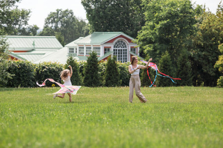 Children in the summer park. A beautiful girl and her mother are flying a kite in the fresh air. Warm family moments or a conceptual image for spending time outdoors.の写真素材