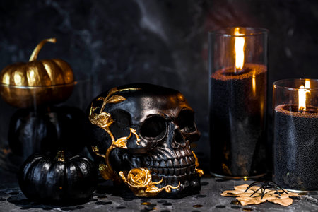 Halloween celebration. Black skull with golden roses, pumpkins, and black candles. Decor for the Day of the Dead or Halloween on a black background.の写真素材
