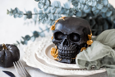 A mysterious black skull with golden roses and pumpkins on serving plates for a Halloween or Day of the Dead party.の写真素材