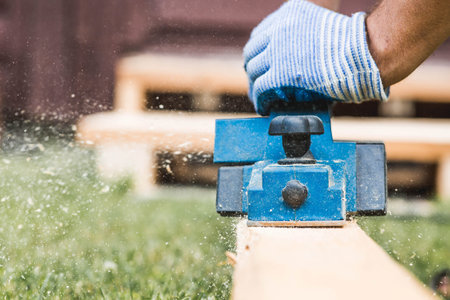 A hand-held electric glider in the hands of a craftsman. A man planning boards with an electric...