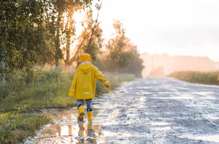 A boy in yellow rubber boots and a raincoat runs through puddles, having fun and playing after it...
