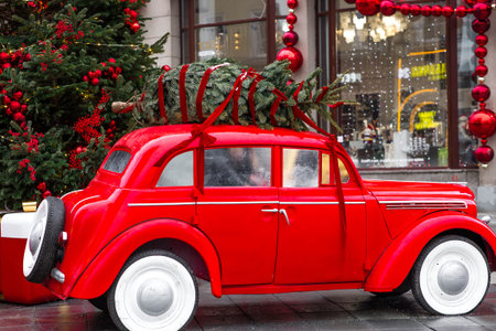 The concept of delivering goods. A Christmas tree is installed on the roof of a vintage red Christmas car. Decorated New Year's Moscow.の写真素材