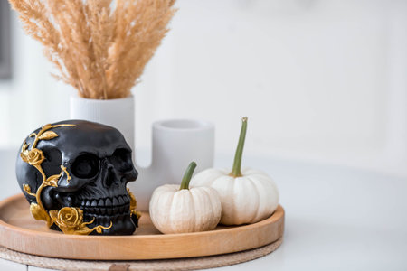 Halloween celebration. A black skull with golden roses and pumpkins on the table. Decor for the Day of the Dead or Halloween in the kitchen interior.の写真素材