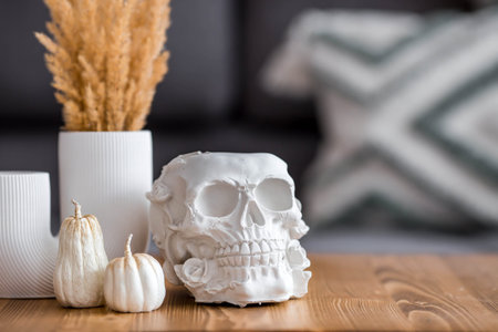 Halloween celebration. A white skull, candles and pumpkins on the table. Decor for the Day of the...