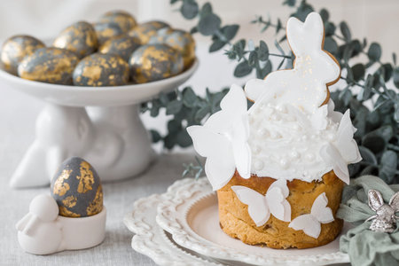Stylish Easter still life. Easter cake with a white rabbit and butterflies, Easter eggs with gold...