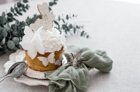 Stylish Easter still life. Easter cake with a white rabbit and butterflies and eucalyptus branches on a white kitchen table. Happy Easter 2026.の写真素材