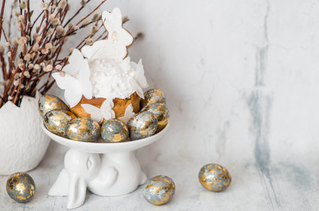 Stylish Easter still life. Easter cake with a white rabbit and butterflies, Easter eggs with gold...