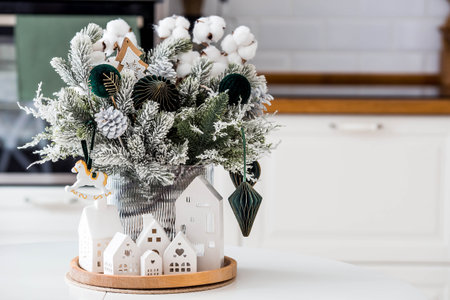 Concept of preparation and decorations for the New Year. A spruce bouquet with green toys and white houses on the kitchen table. Christmas decorations in the interior.の写真素材