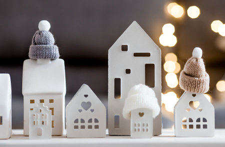 New Year 2026. Models of houses, wearing winter hats with pompoms. Winter. Insulating the house, protecting it from cold and bad weather, and heating the rooms. Creating a festive Christmas atmosphere.の写真素材