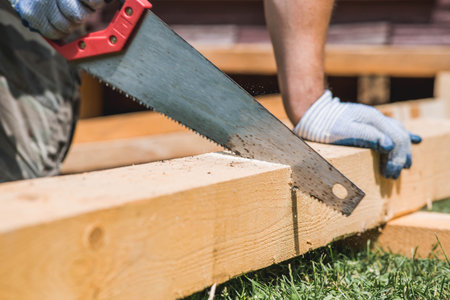 A man sawing a beam with a tool. A hand saw in the hands of a craftsman. Production of wooden products. Construction, wood processing.の写真素材