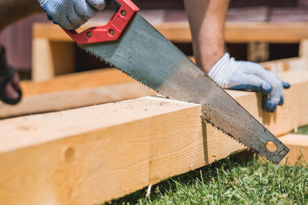 A man sawing a beam with a tool. A hand saw in the hands of a craftsman. Production of wooden products. Construction, wood processing.の写真素材