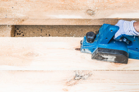 A man is whittling planks with an electric tool. A hand-held electric plane in the hands of a craftsman. Production of wood products. Construction, wood processing.の写真素材