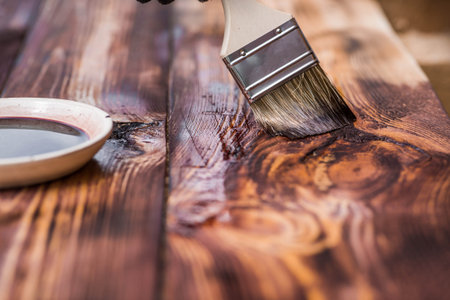 A worker applies a protective wood stain with a brush. The process of protecting and coating wooden boards. The process of restoring parquet flooring.の写真素材