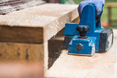 A man is whittling planks with an electric tool. A hand-held electric plane in the hands of a...