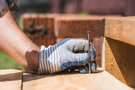A carpenter in cloth protective gloves nails wooden planks. Close-up of a nail hammered into a board.の写真素材
