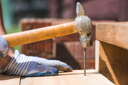 A carpenter in cloth protective gloves nails wooden planks. Close-up of a nail hammered into a board.の写真素材
