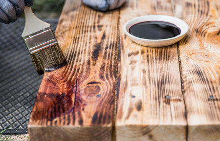 A worker applies a protective wood stain with a brush. The process of protecting and coating wooden boards. The process of restoring parquet flooring.の写真素材