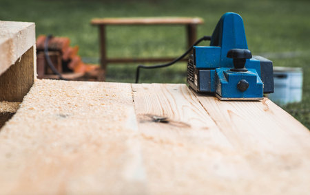 A man is whittling planks with an electric tool. A hand-held electric plane in the hands of a craftsman. Production of wood products. Construction, wood processing.の写真素材