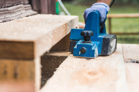 A man is whittling planks with an electric tool. A hand-held electric plane in the hands of a craftsman. Production of wood products. Construction, wood processing.の写真素材