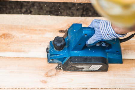 A man is whittling planks with an electric tool. A hand-held electric plane in the hands of a craftsman. Production of wood products. Construction, wood processing.の写真素材