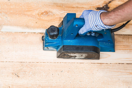 A man is whittling planks with an electric tool. A hand-held electric plane in the hands of a craftsman. Production of wood products. Construction, wood processing.の写真素材