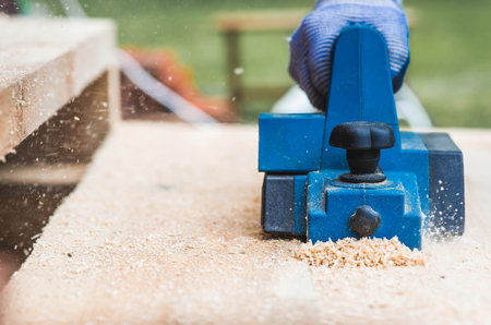 A man is whittling planks with an electric tool. A hand-held electric plane in the hands of a craftsman. Production of wood products. Construction, wood processing.の写真素材