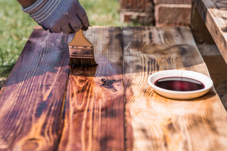 A worker applies a protective wood stain with a brush. The process of protecting and coating wooden boards. The process of restoring parquet flooring.の写真素材