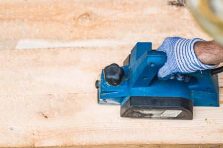 A man is whittling planks with an electric tool. A hand-held electric plane in the hands of a craftsman. Production of wood products. Construction, wood processing.の写真素材