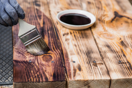 A worker applies a protective wood stain with a brush. The process of protecting and coating wooden boards. The process of restoring parquet flooring.の写真素材