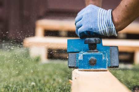A man is whittling planks with an electric tool. A hand-held electric plane in the hands of a...
