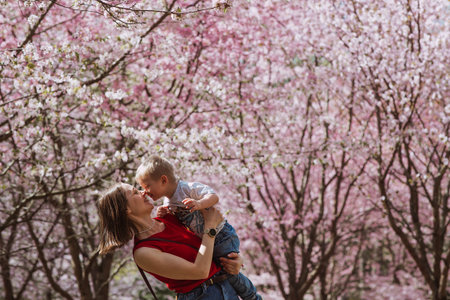 Charming boy and mom in nature in spring among cherry blossom trees. A 2-year-old child is having fun and smiling in his arms. Family and love.の写真素材