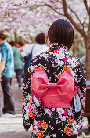 The portrait symbolizes the traditions and culture of the Japanese people. A woman in Japanese clothing with an umbrella in her hand in a cherry blossom garden in the spring.の写真素材