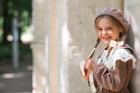 Vintage women's accessories and retro-style clothing. A small, beautiful girl with bows in her hair, in a beige dress and a beret outdoors.の写真素材